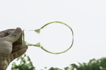 Hand holding light bulb with sunset sky, Use hand hold incandescent lamp for electricity for life concept, Energy saving concept, Incandescent lamp with green nature against the blue skyの写真素材
