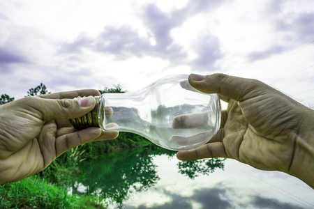 Hand holding light bulb with sunset sky, Use hand hold incandescent lamp for electricity for life concept, Energy saving concept, Incandescent lamp with green nature against the blue skyの写真素材