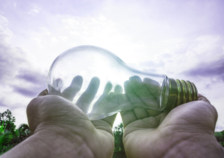 Hand holding light bulb with sunset sky, Use hand hold incandescent lamp for electricity for life...