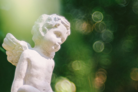 Cupid sculpture in garden the background is blurred bokeh from tree, background for Valentine's day. color toned.の写真素材