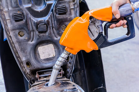 Closeup of hand pumping gasoline fuel in motorcycle at gas station.