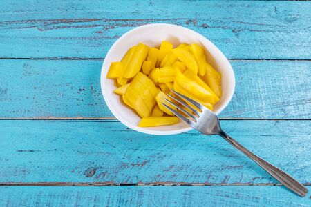 Ripe mango slices in a cup  on a blue wooden table with a fork.の写真素材