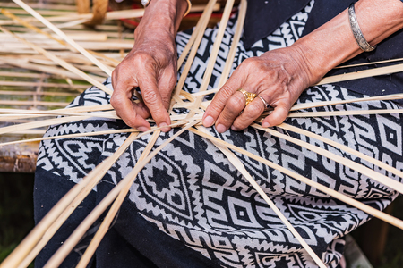Elderly female hands manually weaving bamboo basket.の写真素材