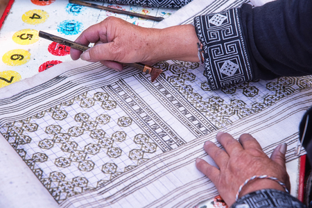 Close-up female hand of Hmong hilltribe draws pattern the wax on white fabric before dyeing in the countryside Thailand.の写真素材