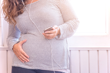 Pregnant woman with smartphone and headphones.の写真素材