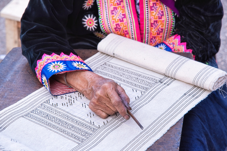 Close-up female hand of Hmong hilltribe draws pattern the wax on white fabric before dyeing in the countryside Thailand.の写真素材