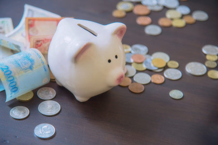 Piggy bank with cash pile on wooden top table, money savings conceptの写真素材