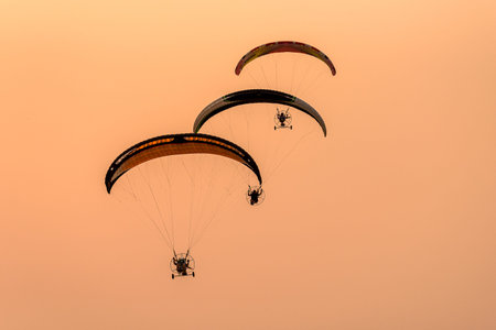 Silhouette of the Paramotor gliding and flying In the air through soft sunlight sky. Paramotor it is...