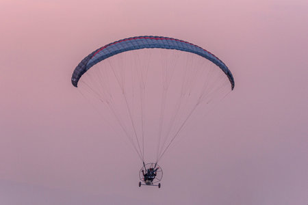 Silhouette of the Paramotor gliding and flying In the air through soft sunlight sky. Paramotor it is...
