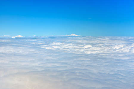 Clouds against blue sky view through an airplane window for a background. Above the clouds, flying in the airの写真素材