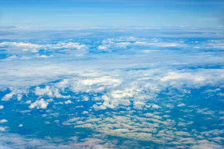 Clouds against blue sky view through an airplane window for a background. Above the clouds, flying in the airの写真素材