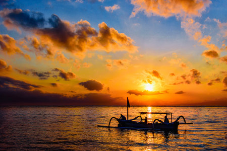 Beautiful sunrise scenery with Jukung is traditional balinese fishing boats at Karang Beach, Sanur, Bali, Indonesia.Fishing boat on sea beach with sunrise background.の写真素材
