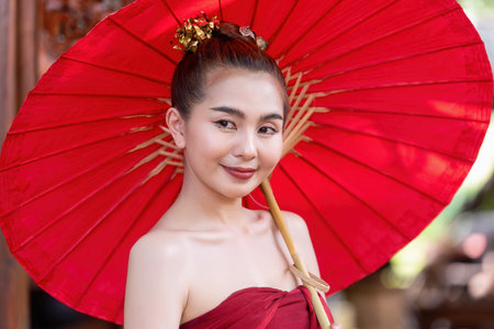 Thai woman dressed in traditional Northern Thailand culture costume holding a paper umbrella....