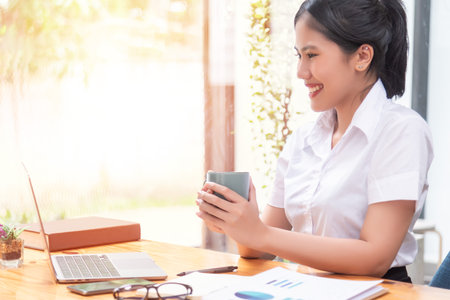 Asian businesswoman holding a cup of coffee relaxing sitting in the office.の写真素材