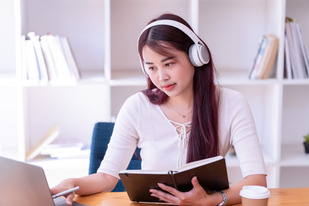 Asian women wear headphones listen to music relax and write notes. Pretty woman learning online. She puts on headphones and works.の写真素材