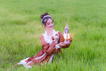 Young girl holding a lantern in the green meadow. Girl enjoys and cheerfully in the fieldの写真素材