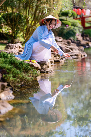 A young woman wearing a traditional Vietnamese Ao Dai dress is happy and cheerful in the park. Ao dai is a traditional costume for Vietnamese women.の写真素材