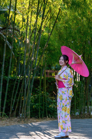 A young woman wearing a Japanese traditional kimono or yukata holding an umbrella is happy and cheerful in the park. Japanese traditional summer dress.の写真素材