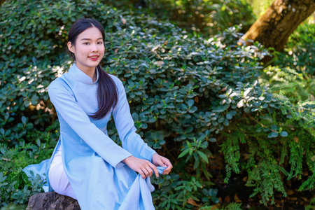 A young woman wearing a traditional Vietnamese Ao Dai dress is happy and cheerful in the park. Ao...