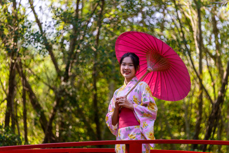 A young woman wearing a Japanese traditional kimono or yukata holding an umbrella is happy and cheerful in the park. Japanese traditional summer dress.の写真素材