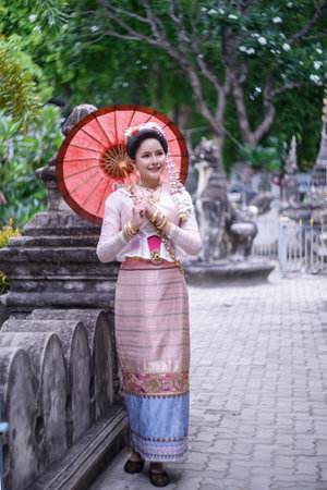 A young Thai woman dressed in traditional Northern Thailand culture costume visits a temple in Chiang Mai, Thailand. Asian young Women in traditional costumes at the Thai Templeの写真素材