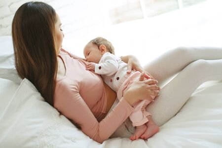 Beautiful woman breastfeeding her baby in a cozy house on the bed.の写真素材