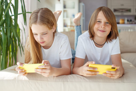 Children at home each play their own game. Brother and sister are playing at home. The child plays...