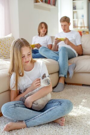 Children at home each play their own game. Brother and sister are playing at home. The child plays on the phone. A child is playing with a cat.の写真素材