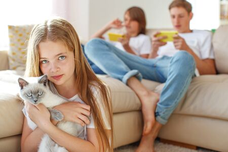 Children at home each play their own game. Brother and sister are playing at home. The child plays on the phone. A child is playing with a cat.の写真素材