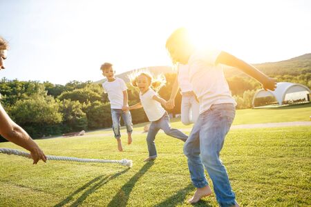 A group of children have fun playing in nature. Children jump over the rope. Warm summer evening with sunset light.の写真素材
