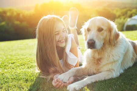 A child with a dog in nature. girl playing with a dog on green grass at sunset time.の写真素材
