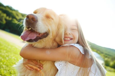 A child with a dog in nature. girl playing with a dog on green grass at sunset time.の写真素材