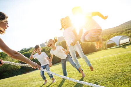 A group of children have fun playing in nature. Children jump over the rope. Warm summer evening with sunset light.の写真素材