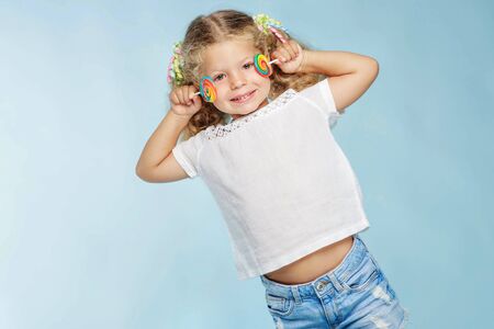 A child with a candy. Little girl with a round candy in the studio on a blue background.の写真素材