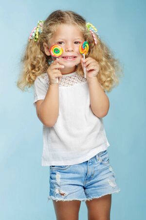 A child with a candy. Little girl with a round candy in the studio on a blue background.の写真素材