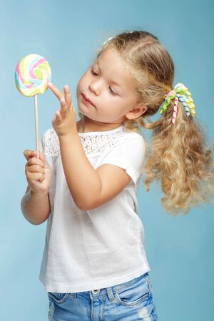 A child with a candy. Little girl with a round candy in the studio on a blue background.の写真素材