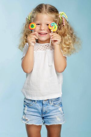 A child with a candy. Little girl with a round candy in the studio on a blue background.の写真素材
