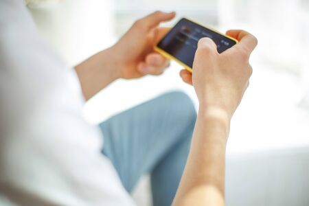 A young man with a phone in his hands is playing. A teenager plays on the phone at home.の写真素材