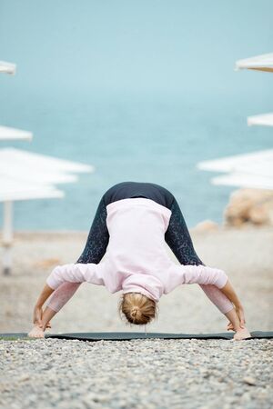 A woman practices yoga by the sea. Yoga girl. Young beautiful woman doing yoga poses in nature.の写真素材