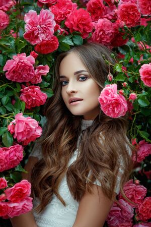 Beautiful portrait of a woman in poses. A brunette woman is standing next to roses in nature.の写真素材