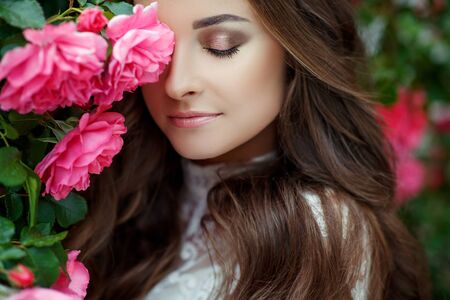 Beautiful portrait of a woman in poses. A brunette woman is standing next to roses in nature.の写真素材