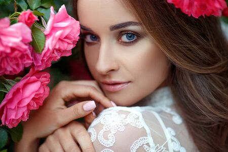 Beautiful portrait of a woman in poses. A brunette woman is standing next to roses in nature.の写真素材