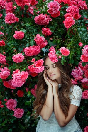Beautiful portrait of a woman in poses. A brunette woman is standing next to roses in nature.の写真素材