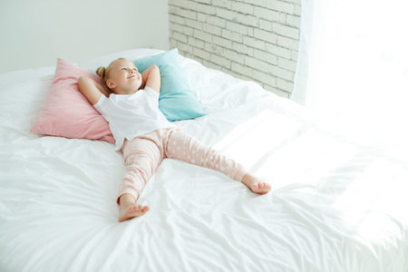 Little girl in bed with white linen. A child at home in the morning wakes up in his room. High...