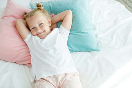 Little girl in bed with white linen. A child at home in the morning wakes up in his room. High quality photo.の写真素材
