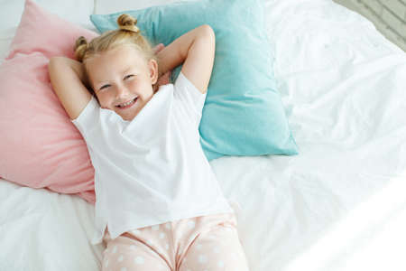 Little girl in bed with white linen. A child at home in the morning wakes up in his room. High quality photo.の写真素材