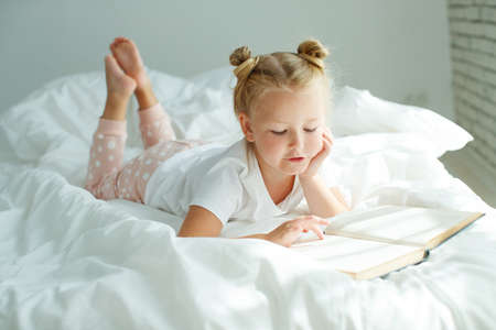 Little girl in bed with white linen. A child at home in the morning wakes up in his room. High quality photo.の写真素材
