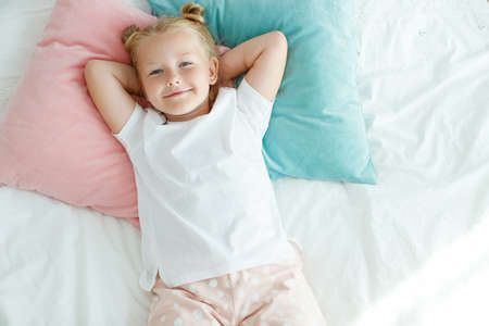 Little girl in bed with white linen. A child at home in the morning wakes up in his room. High quality photo.の写真素材