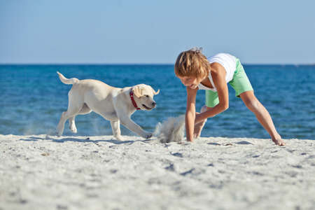 Happy boy playing with his dog on the seashore against the blue sky. Best friends have fun on vacation, play on the sand against the sea. High quality photo.の写真素材