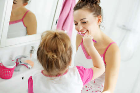 Mother and her daughter brush their teeth with toothbrushes in the bathroom at home. Mom and baby girl in home clothes. High quality photo.の写真素材